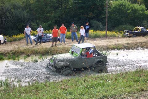 1979 Ford F-150 - A modified jeep navigates a muddy track while onlookers observe the off-road event.