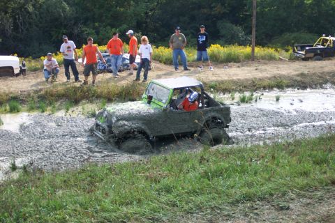 1979 Ford F-150 - An off-road vehicle navigates a muddy obstacle course, with spectators watching from the bank.