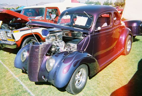 1972 Ford Ranchero - A custom purple hot rod coupe with flame paint and a prominent V8 engine is displayed on a grassy field.