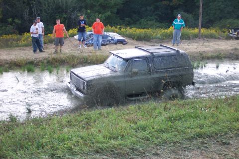 1979 Ford F-150 - A group of people watch as a muddy SUV struggles through a water-filled ditch.