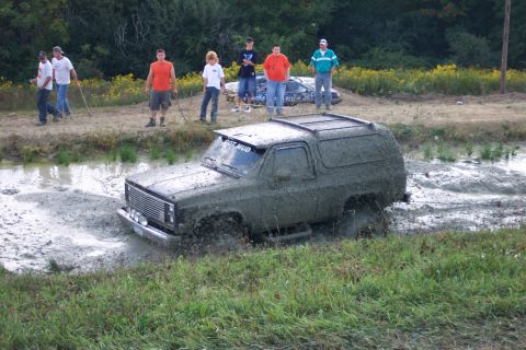 1979 Ford F-150 - A muddy SUV navigates a water-filled ditch while onlookers watch from the bank.