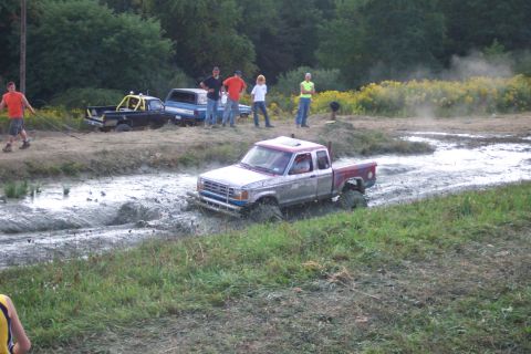 1979 Ford F-150 - A pickup truck navigates a muddy track during an event, with other vehicles and spectators in the background.
