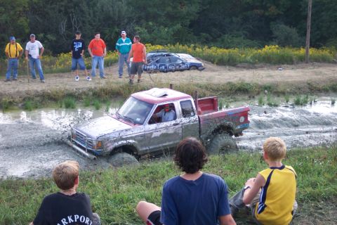 1979 Ford F-150 - A pickup truck is stuck in a mud pit during an off-road event, with onlookers observing the scene.