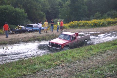 1979 Ford F-150 - Several trucks are stuck in a muddy track with onlookers observing the scene.