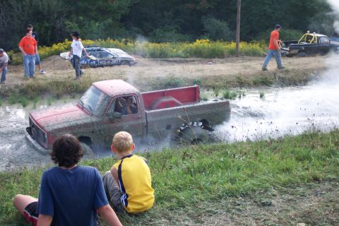 1979 Ford F-150 - A red 1979 Ford F-150 navigates a muddy obstacle course while onlookers observe the action.