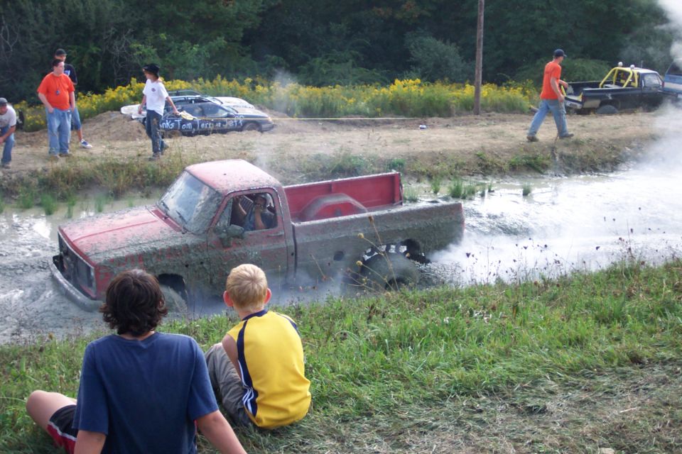 Red 1979 Ford F-150 stuck in mud pit with spectators watching