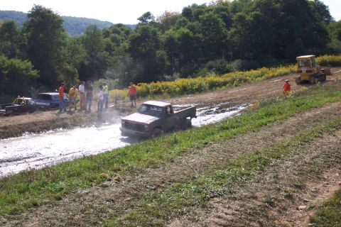 1979 Ford F-150 - Multiple trucks navigate a muddy track during an event, with onlookers and a bulldozer present.
