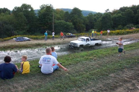 1979 Ford F-150 - Spectators watch as a white pickup truck navigates a muddy track during an off-road event.