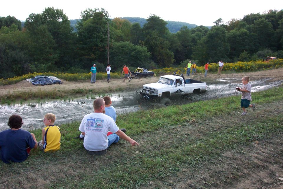 White pickup truck driving through mud pit with people watching