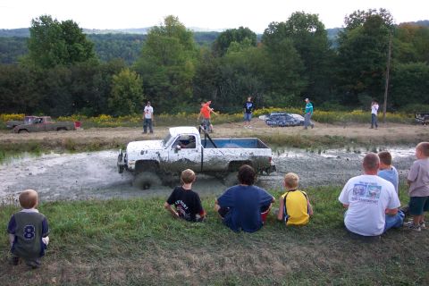 1979 Ford F-150 - A white pickup truck is stuck in a mud pit while spectators watch.