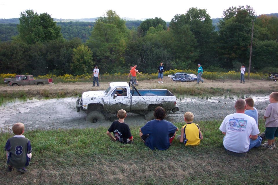 White pickup truck stuck in mud, viewed from the side. Mud covers the vehicle