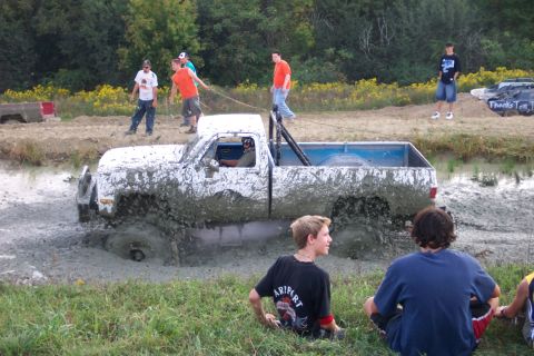 1979 Ford F-150 - A white pickup truck is stuck in a mud pit during an event, with spectators observing.