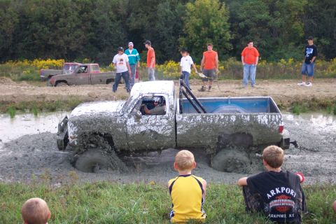 1979 Ford F-150 - Two trucks are stuck in the mud during an off-road event, with spectators watching.