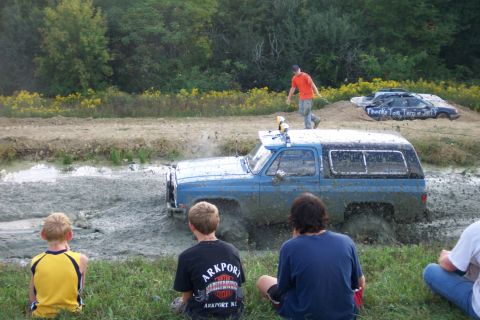 1979 Ford F-150 - A blue SUV is stuck in a mud pit while spectators watch the off-road event.