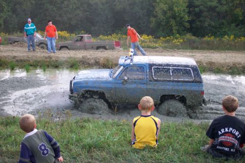 1979 Ford F-150 - A blue SUV is stuck in the mud while people watch from the side.