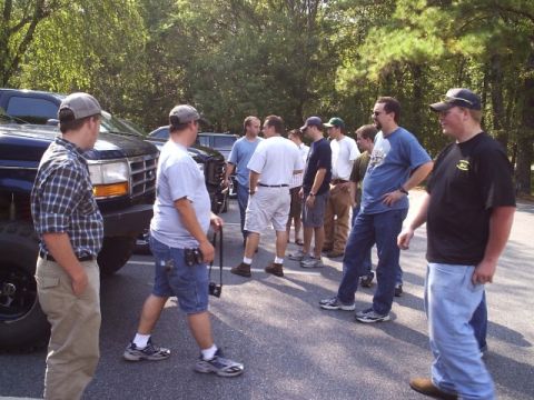 1989 Ford Bronco - Several men gather around a large black truck parked in an outdoor lot on a sunny day.