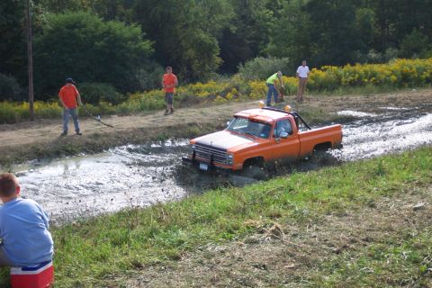 1979 Ford F-150 - An orange pickup truck navigates a muddy track, with several people observing the scene.