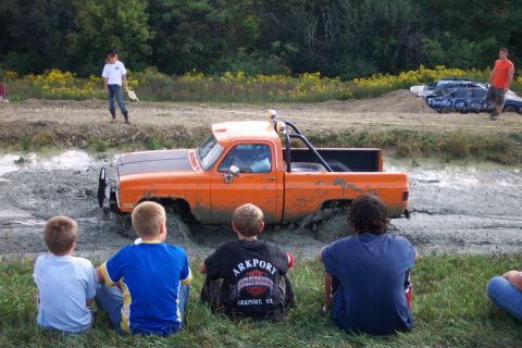 1979 Ford F-150 - A crowd watches as an orange pickup truck struggles in a mud pit.