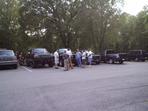 1989 Ford Bronco - Several vehicles are parked in a lot, including a black Ford Bronco and pickup trucks.