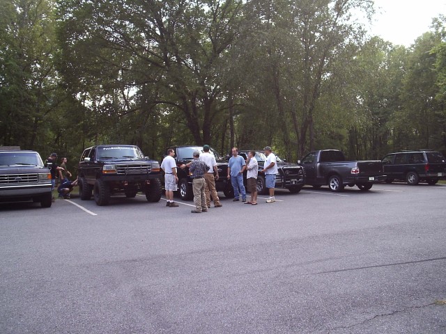 People gathered in parking lot beside row of lifted Ford trucks at cookout