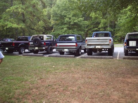 1989 Ford Bronco - Multiple Ford trucks and a Bronco are parked in a lot on a sunny day.