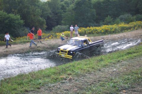1979 Ford F-150 - A pickup truck navigates a muddy track, kicking up water and mud as onlookers observe from the side.