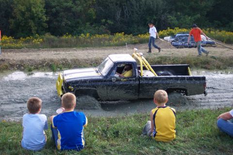 1979 Ford F-150 - A black pickup truck is stuck in the mud during an event, with onlookers watching from the side.
