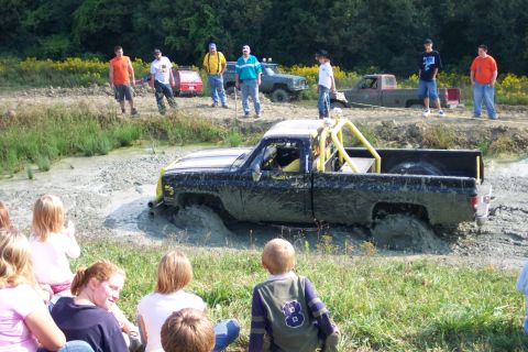 1979 Ford F-150 - A crowd watches as a modified pickup truck gets stuck in thick mud during an off-road event.