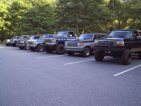 1989 Ford Bronco - A lineup of Ford Broncos and trucks are parked in a lot on a sunny day.