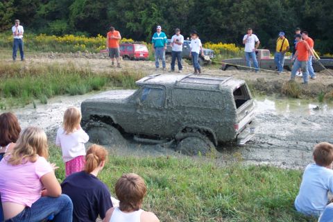 1979 Ford F-150 - A group of people watch as an SUV is stuck deep in the mud during an off-road event.