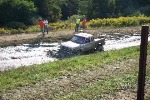 1979 Ford F-150 - A silver pickup truck is stuck in a mud pit with people watching from the side.