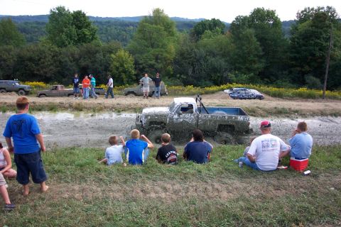 1979 Ford F-150 - Spectators watch a mud-covered pickup truck stuck in a mud pit during an event.