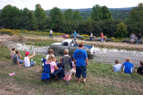 1979 Ford F-150 - Spectators watch as trucks navigate a muddy course during an outdoor event.