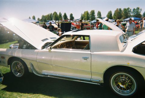 1972 Ford Ranchero - A classic white coupe is displayed with its hood open at an outdoor car show, surrounded by other vehicles and attendees.