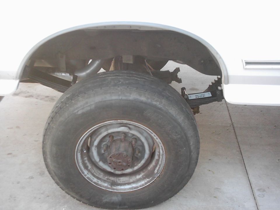 Rear wheel, leaf spring suspension, and exhaust pipe on a white vehicle