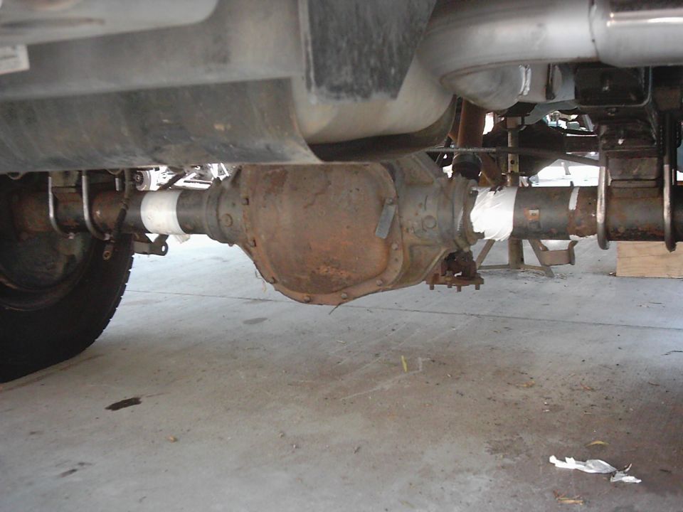 underneath view of a rusty rear axle assembly with white tape on the driveshaft
