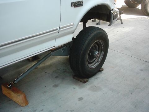 1978 Ford Bronco - A white Ford Bronco is shown from the side, lifted on wooden blocks and mechanical supports, with its front wheel visible.