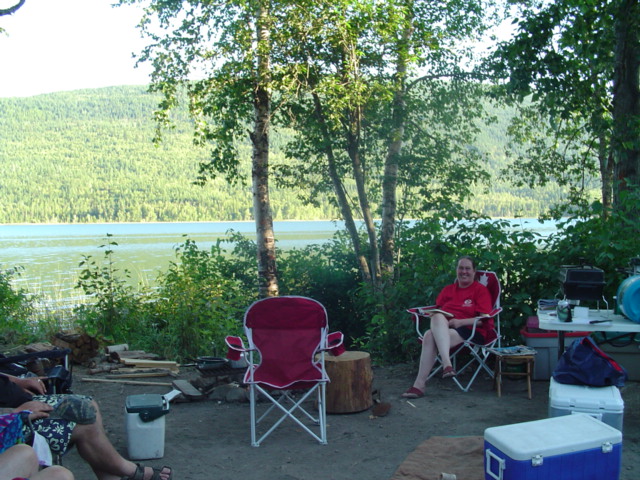 Lakeside campsite with red folding chairs, coolers and a fire ring under birch trees