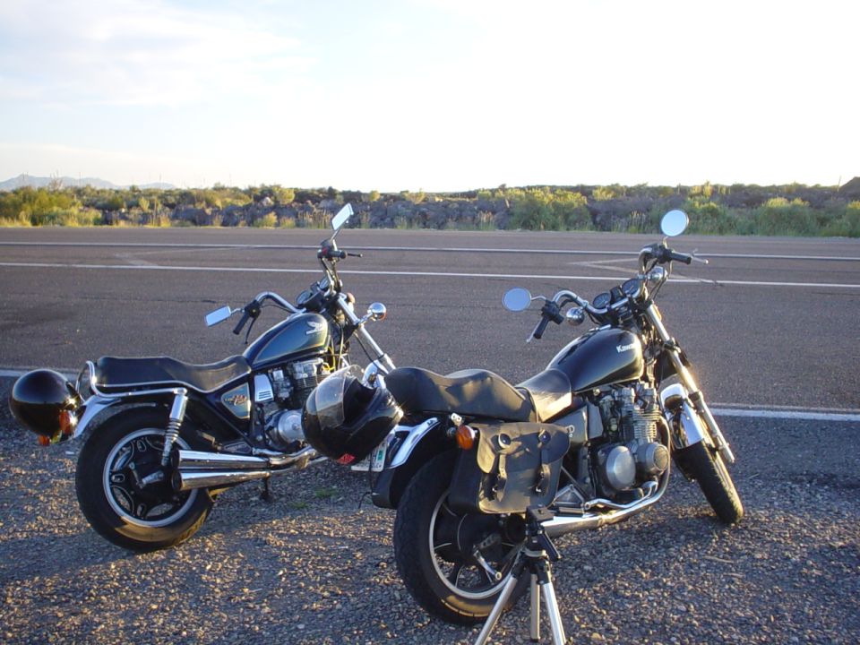 Two motorcycles parked on asphalt with a distant landscape