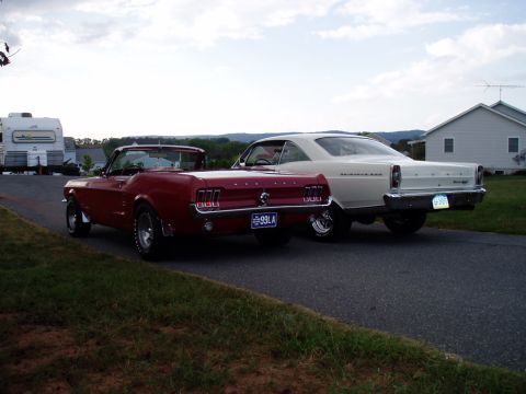 1967 Ford Mustang - Two vintage cars, a red convertible and a white coupe, are parked side-by-side on a paved surface.