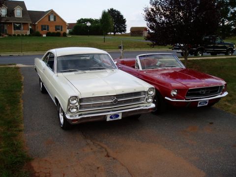 1967 Ford Mustang - Two classic Ford cars, a 1967 Mustang convertible and a white Fairlane, parked in a suburban driveway.