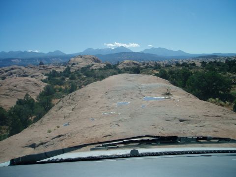 2000 Ford E350 - Driver's-eye view over a light-colored hood and black cowl at the crest of a slickrock dome, with puddles standing in shallow pockets in th…