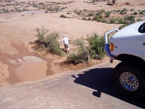 2000 Ford E350 - White Ford 4x4 tipped down a red slickrock slope in the desert, with only the dust-coated right front corner in frame: tubular grille guard…