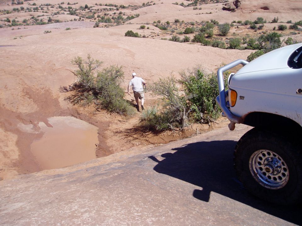 White Ford 4x4 front corner with brush guard on red slickrock, man spotting ahead