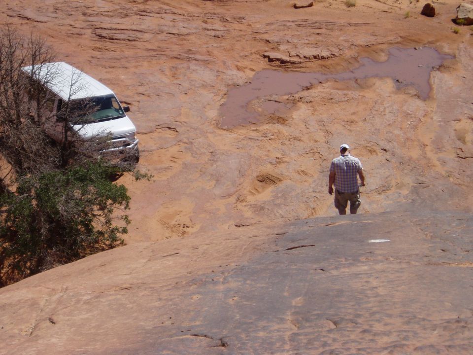 White full-size van parked in red slickrock bowl with man walking the trail nearby