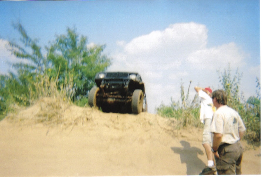 Mud-covered black off-road vehicle on a sandy incline with two people watching
