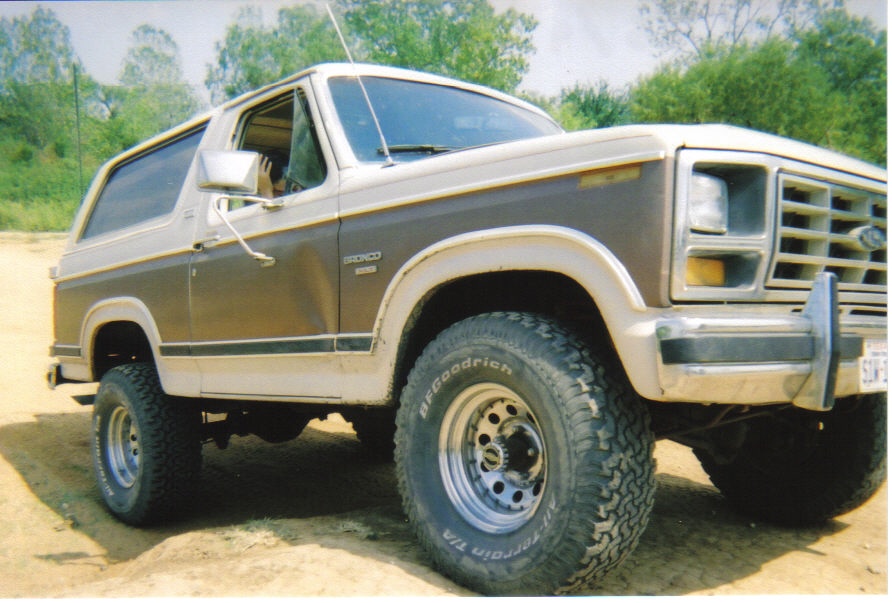 1982 Ford Bronco, two-tone brown and white, parked on dirt with trees in background