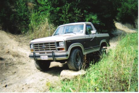 1982 Ford Bronco - This two-tone brown and white Ford Bronco navigates an off-road trail with rocky terrain.