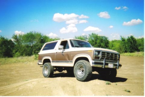 1982 Ford Bronco - This two-tone Ford Bronco sits on a dirt lot under a bright blue sky with scattered clouds.