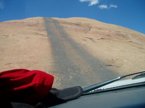 2000 Ford E350 - Through-the-windshield view from inside a vehicle facing a steep slickrock dome, with two dark tire-rubber streaks marking the climb line u…